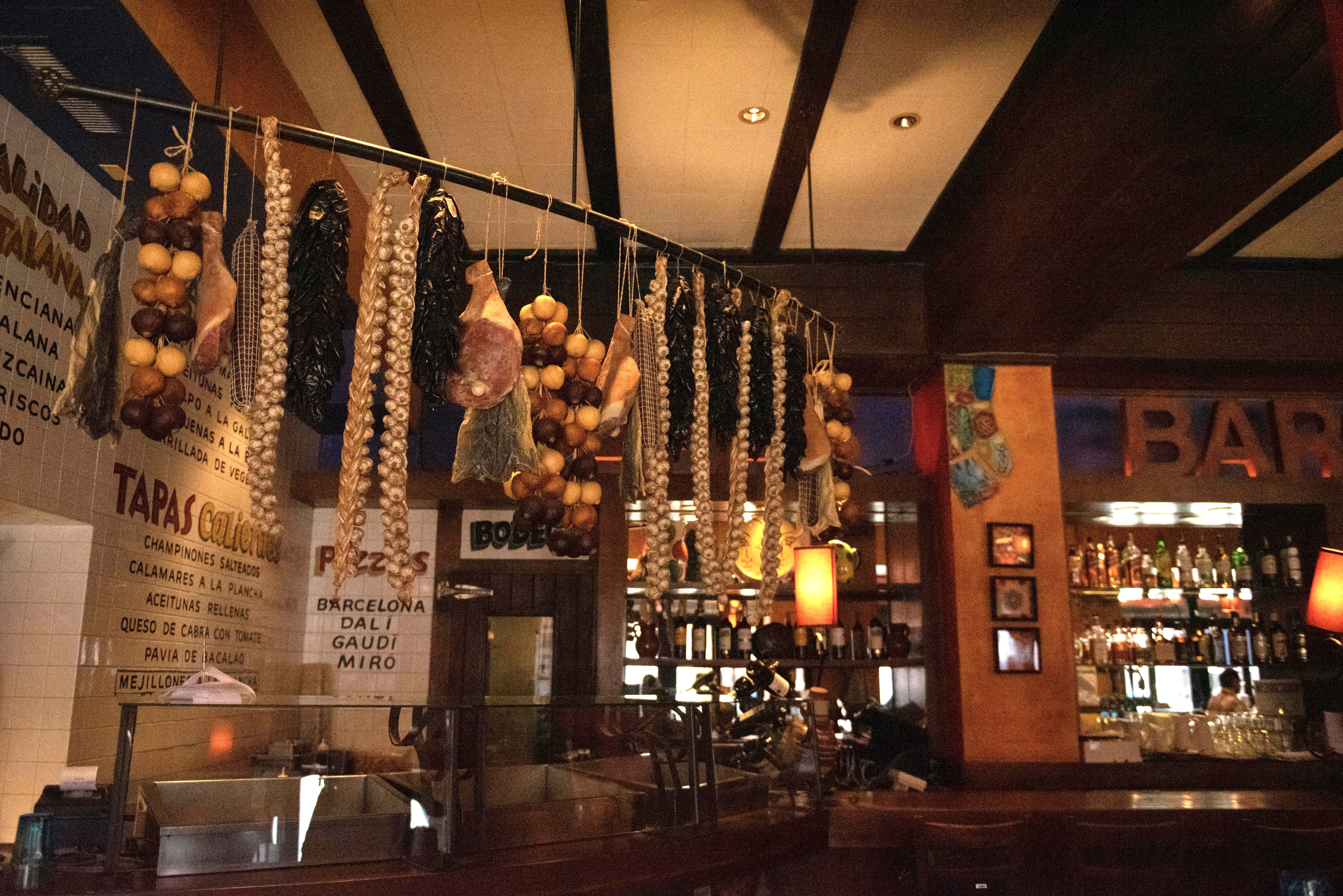  Assorted meats and fruits hang from the ceiling above a bar.