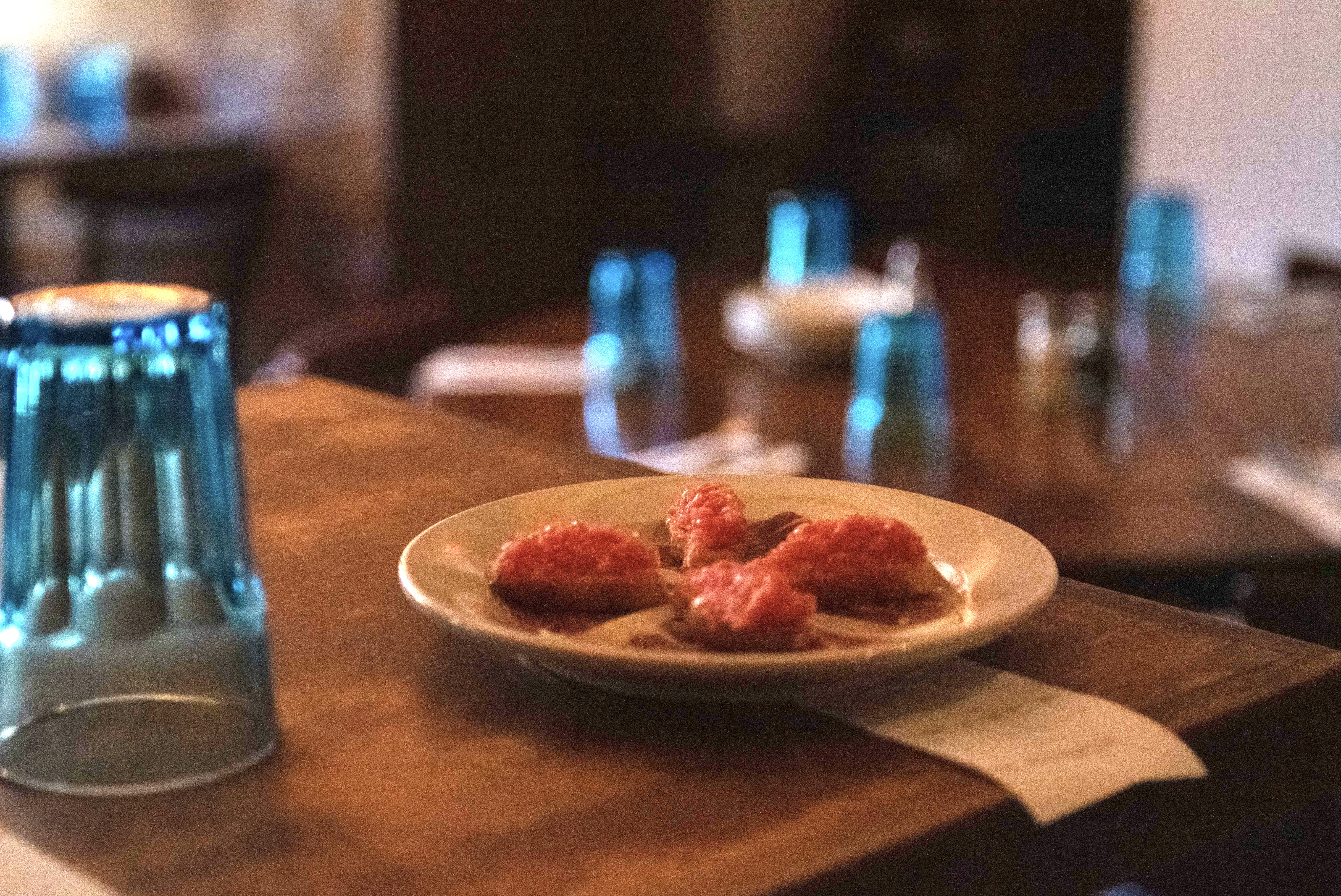 Blue glass cups sit upside down on a brown table with a plate of meat.