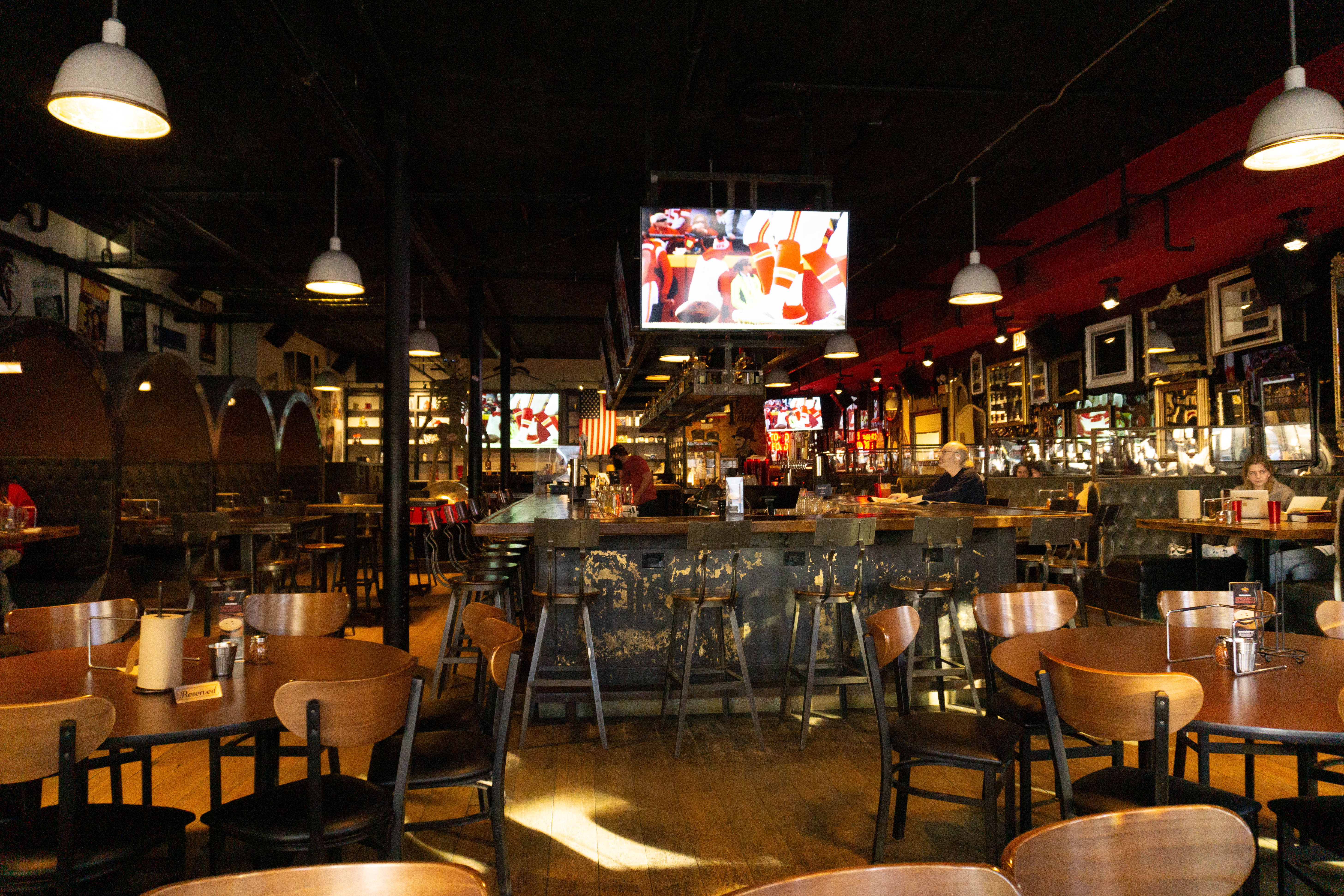 A TV plays in a room with a bar and wooden tables.