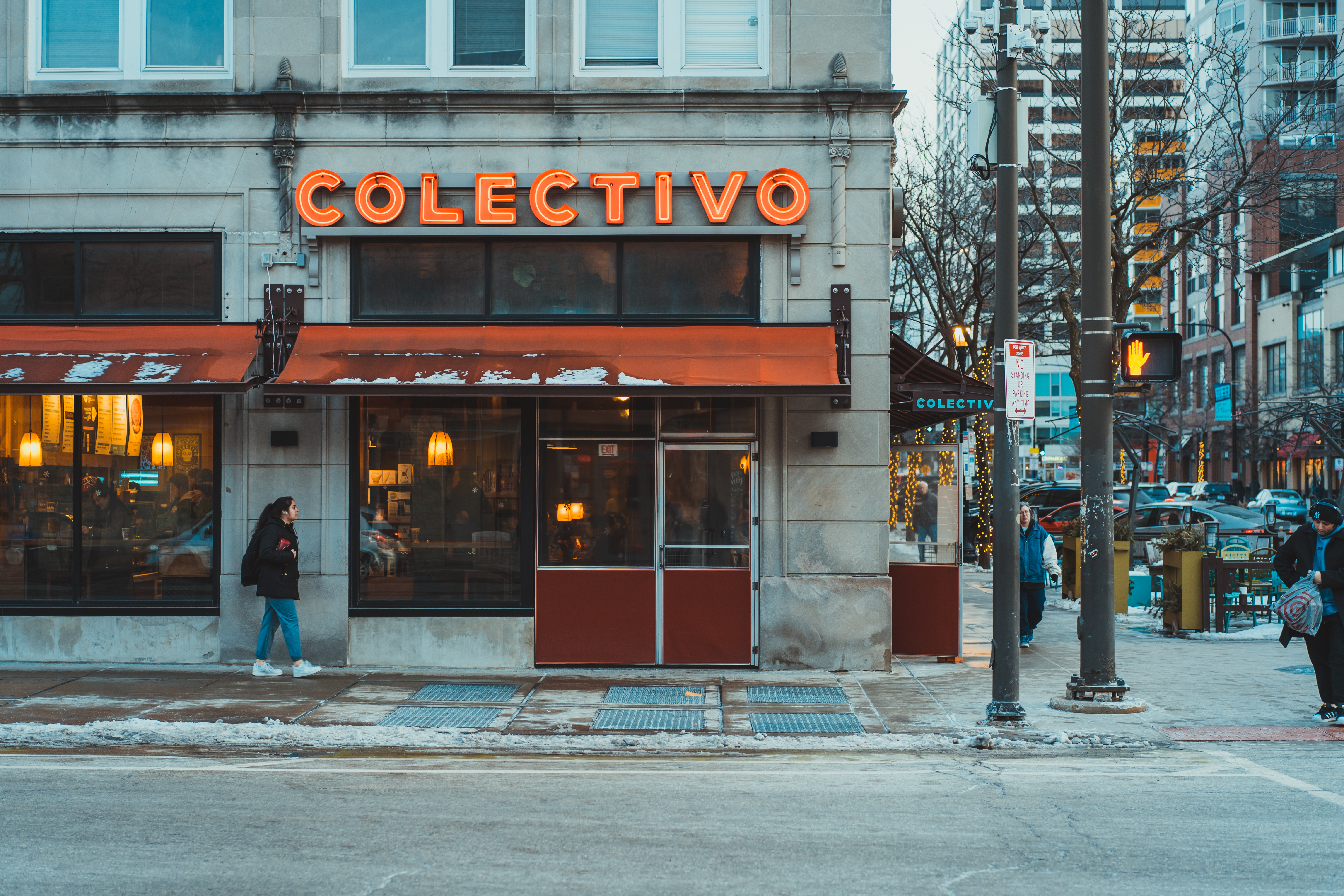 A red sign reading “Collectivo” shines over a pedestrian walking in snow. 