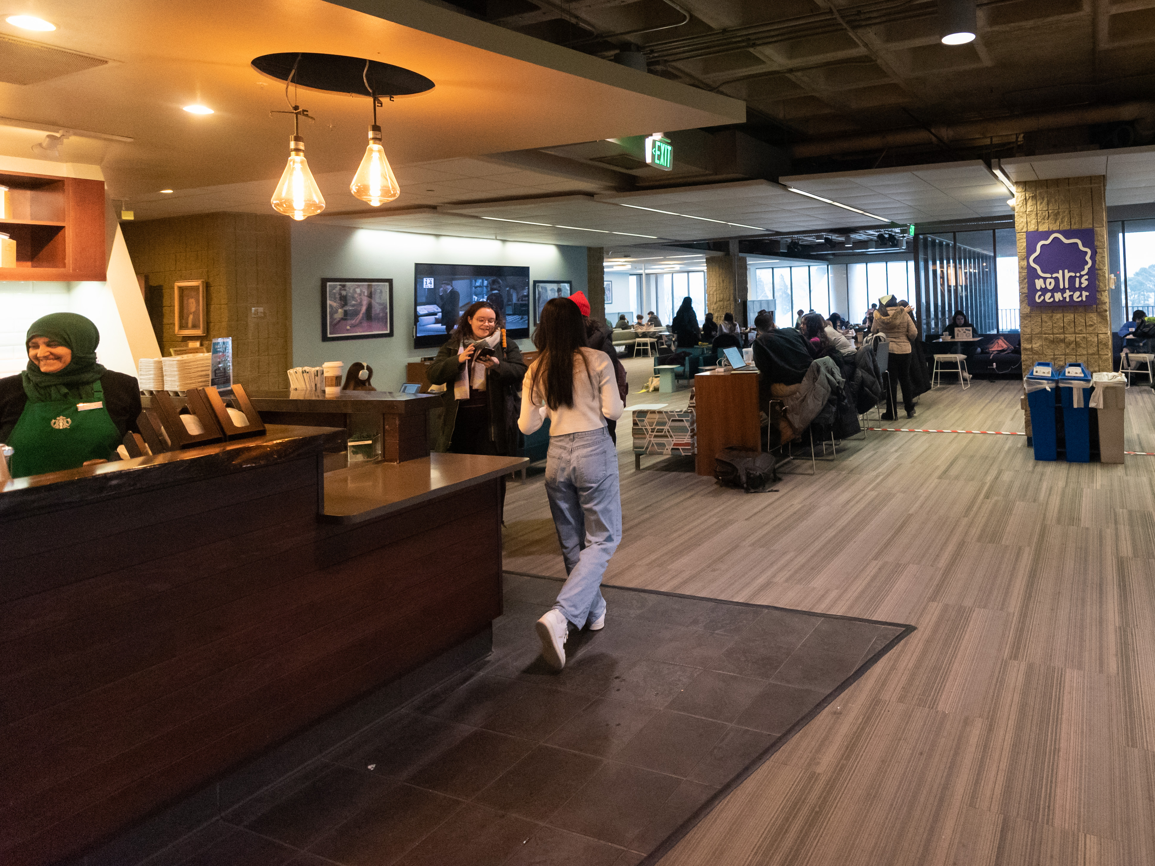 Norris University Starbucks with people studying at tables, waiting for drinks, and workers making drinks.