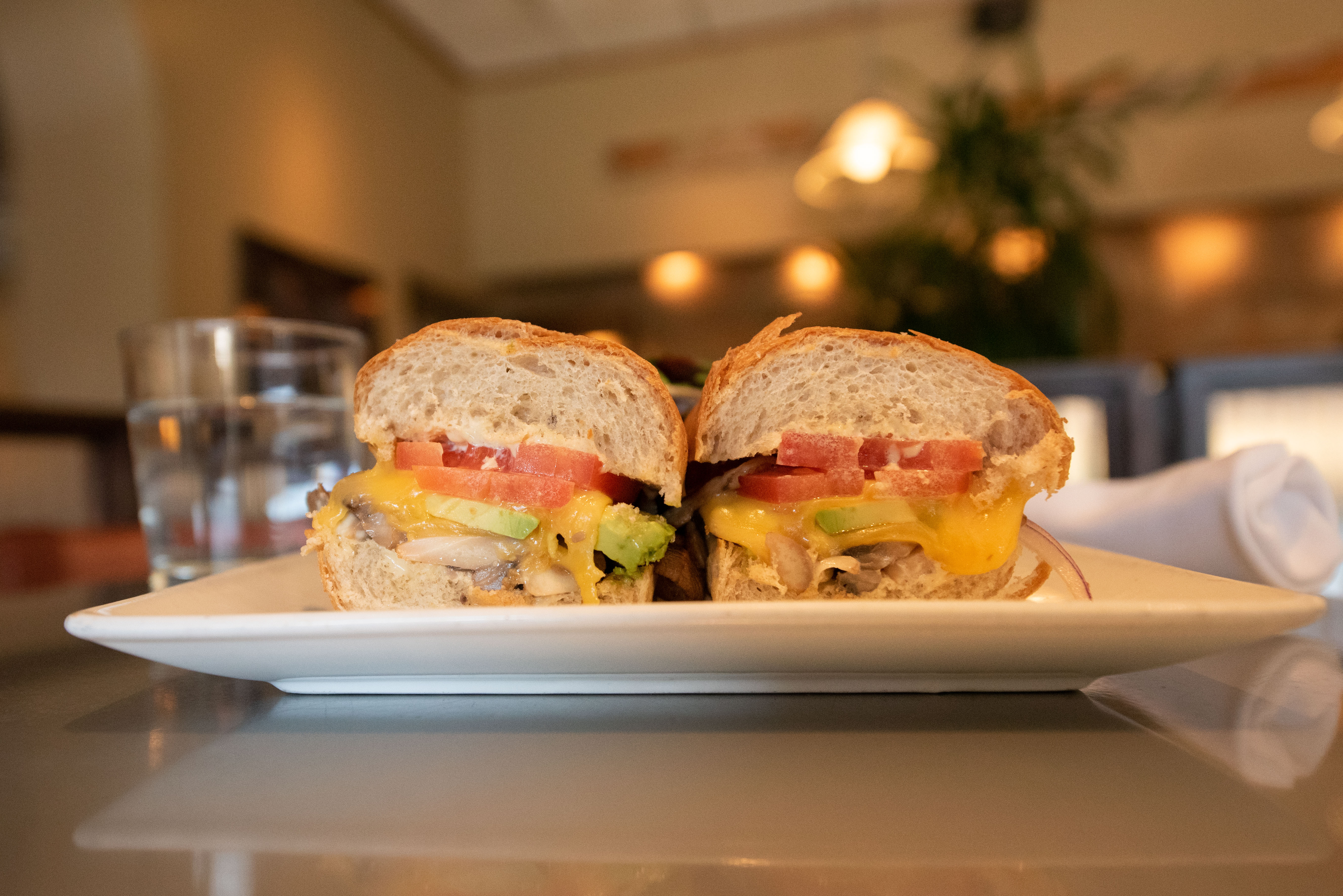 A sandwich with tomato, cheese, avocado and mushroom sits on a plate.