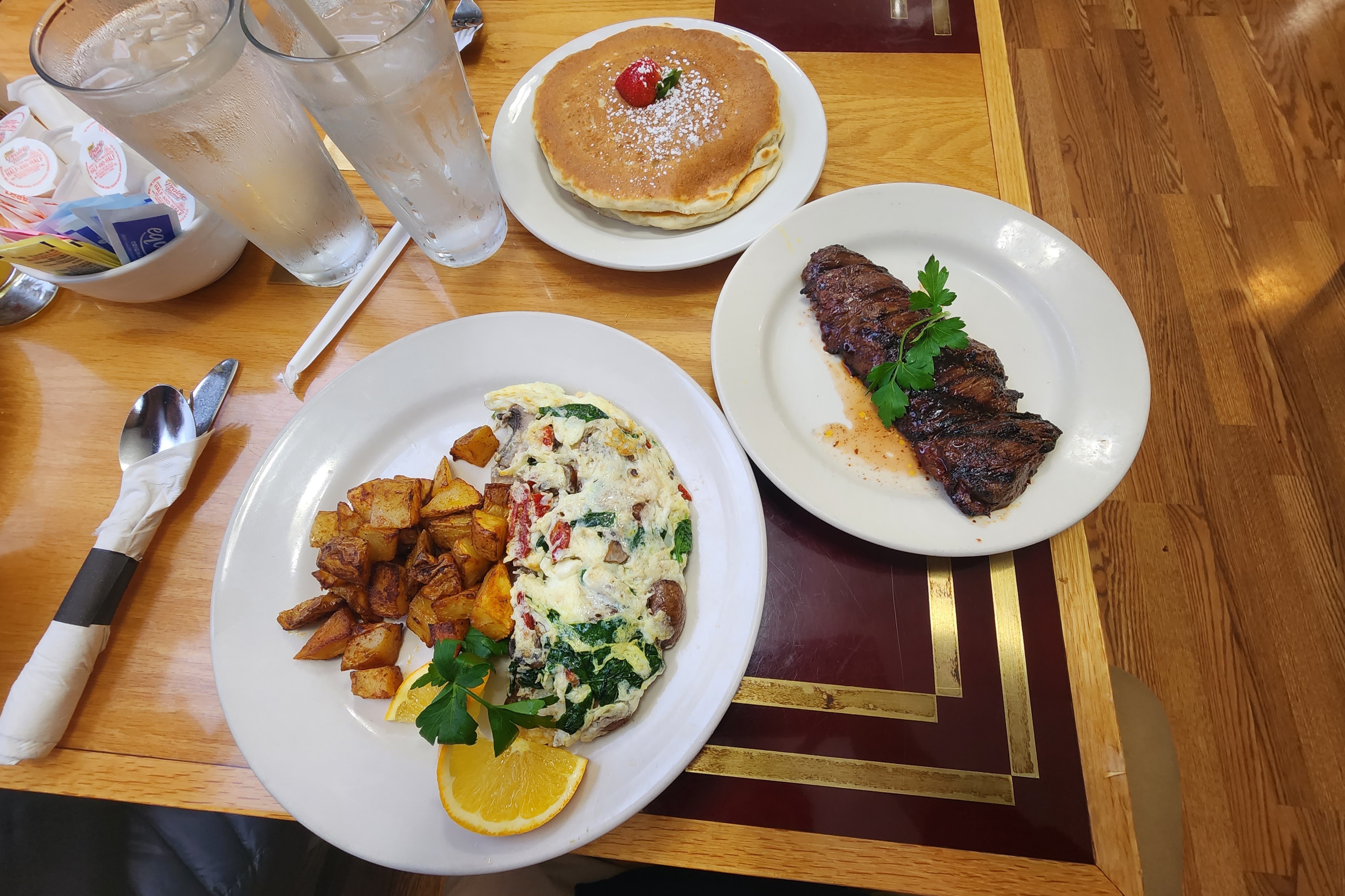 A plate with an omelet, steak, potatoes and pancakes.