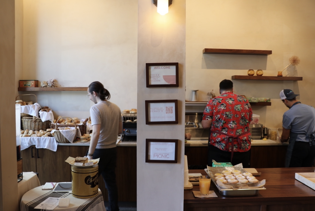 Three people prepare bagel orders behind a counter.