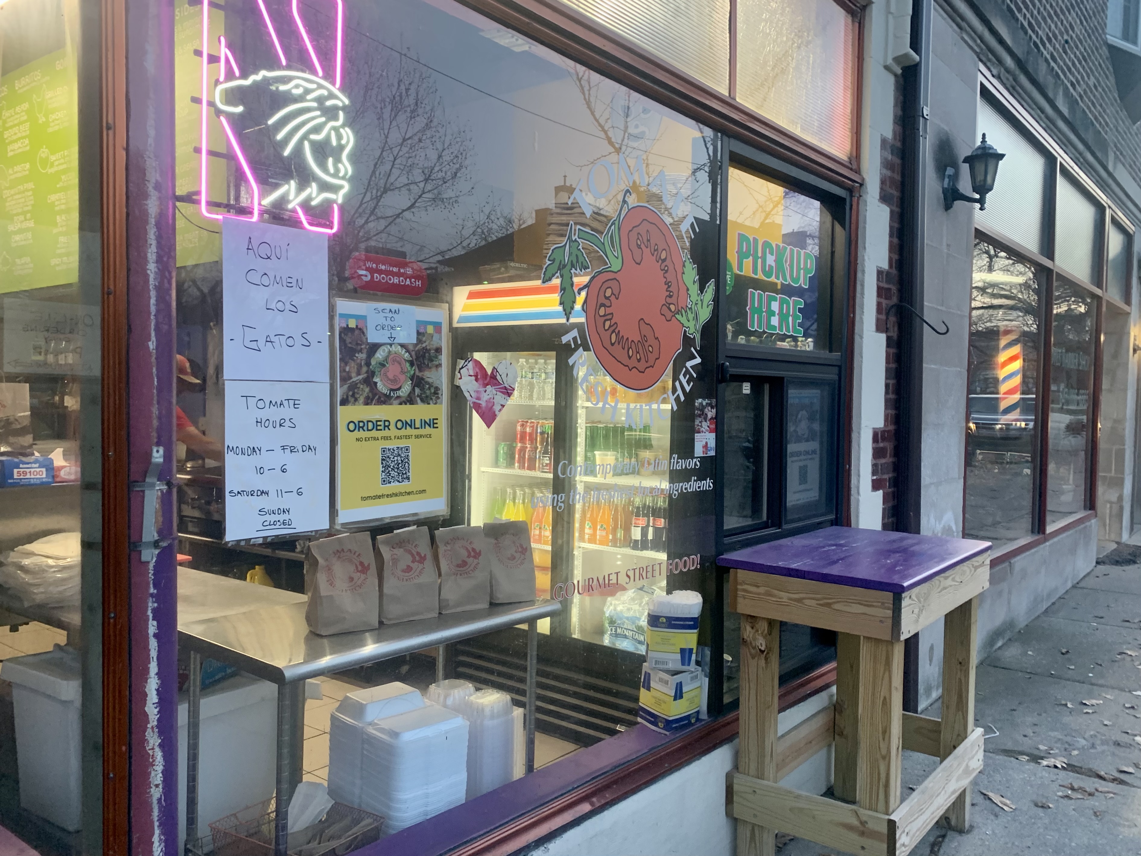 Tomate Fresh Kitchen storefront and pickup window. Signs and directions to order online are displayed next to the company's tomato logo. 