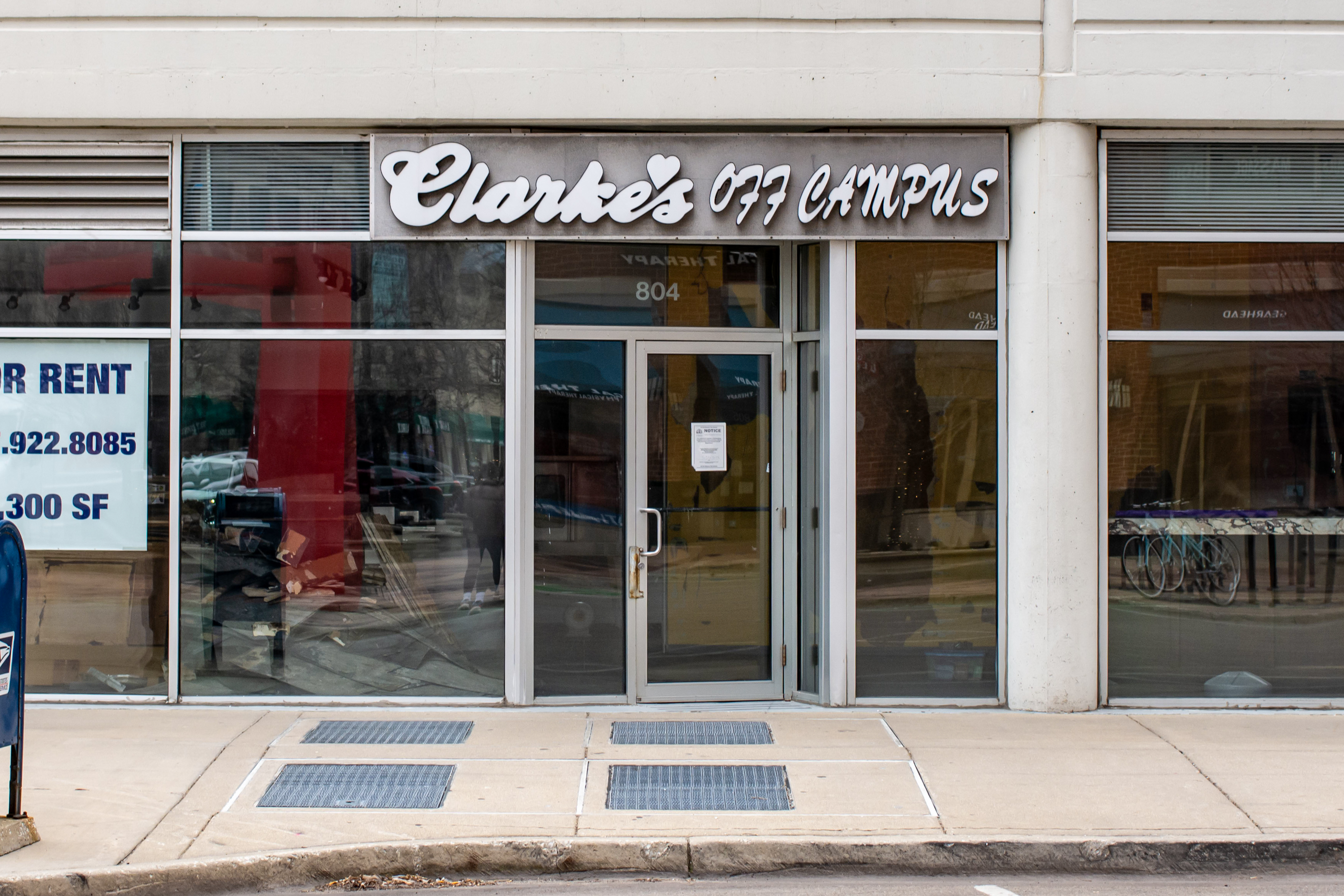 White lettering reads “Clarke’s Off Campus” over a building with floor-to-ceiling windows.