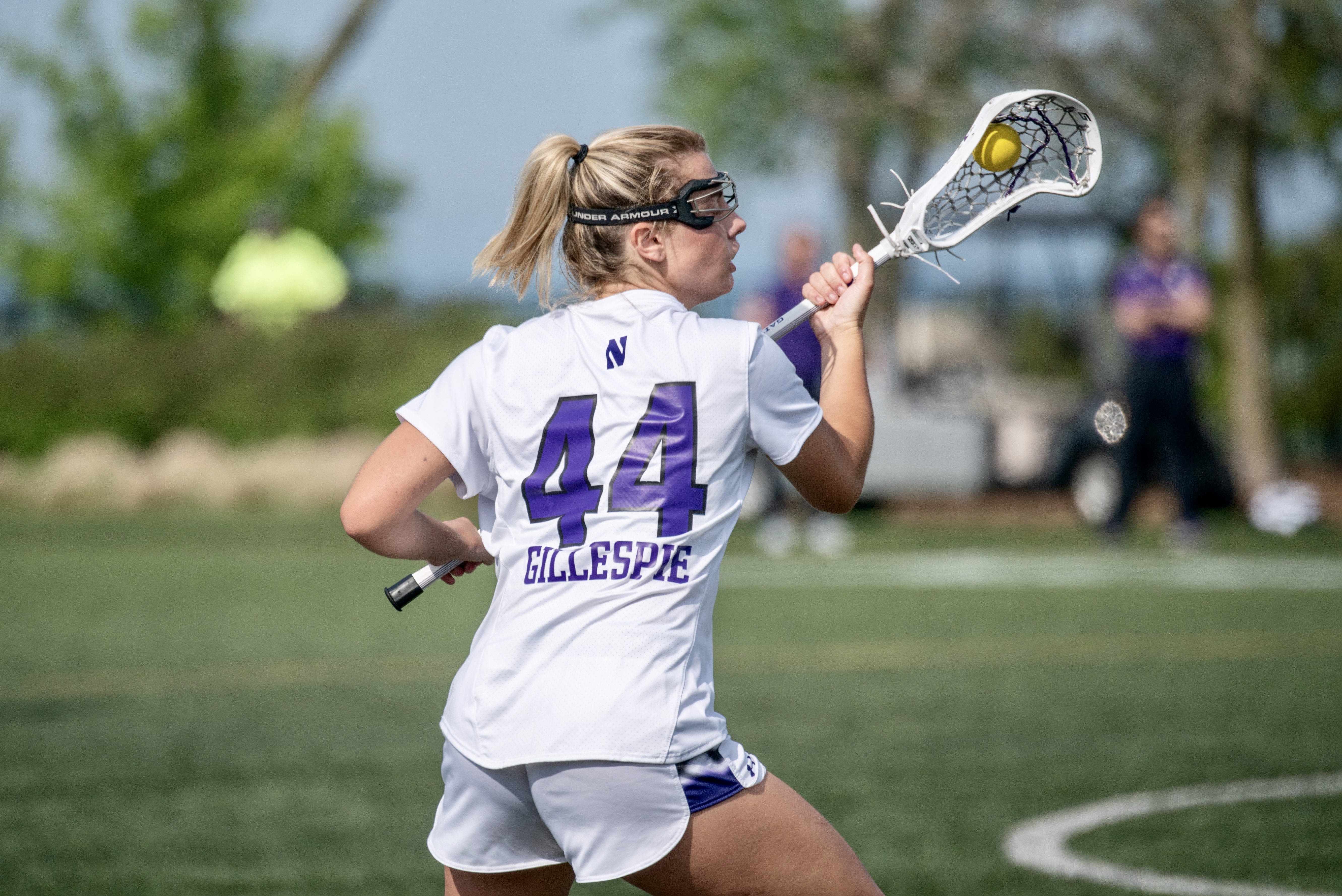 An athelete in white jersey holds a lacrosse stick