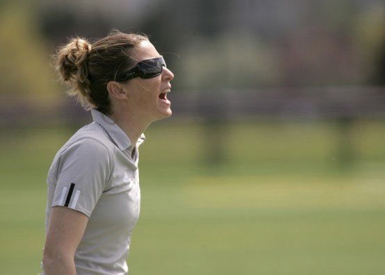 A woman in a gray shirt yells in a grass field.