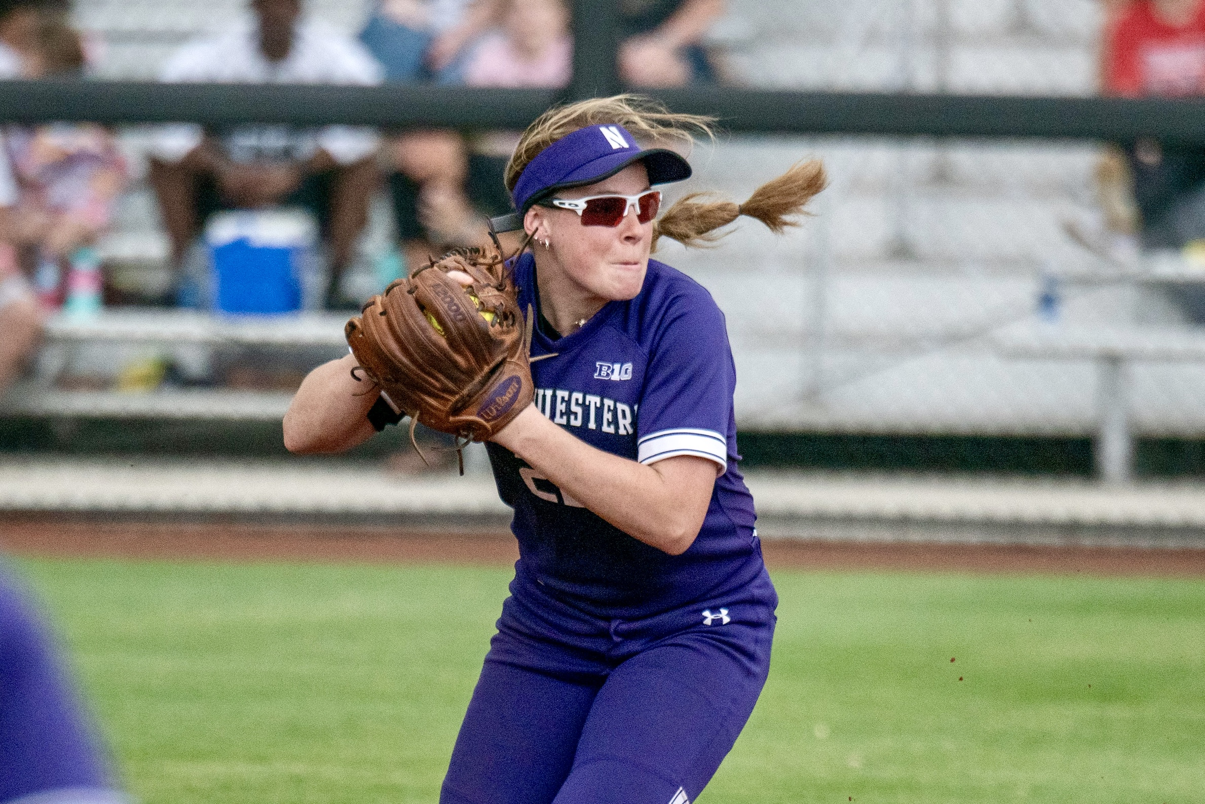 An athelete in purple jersey holds a softball with the gloves.