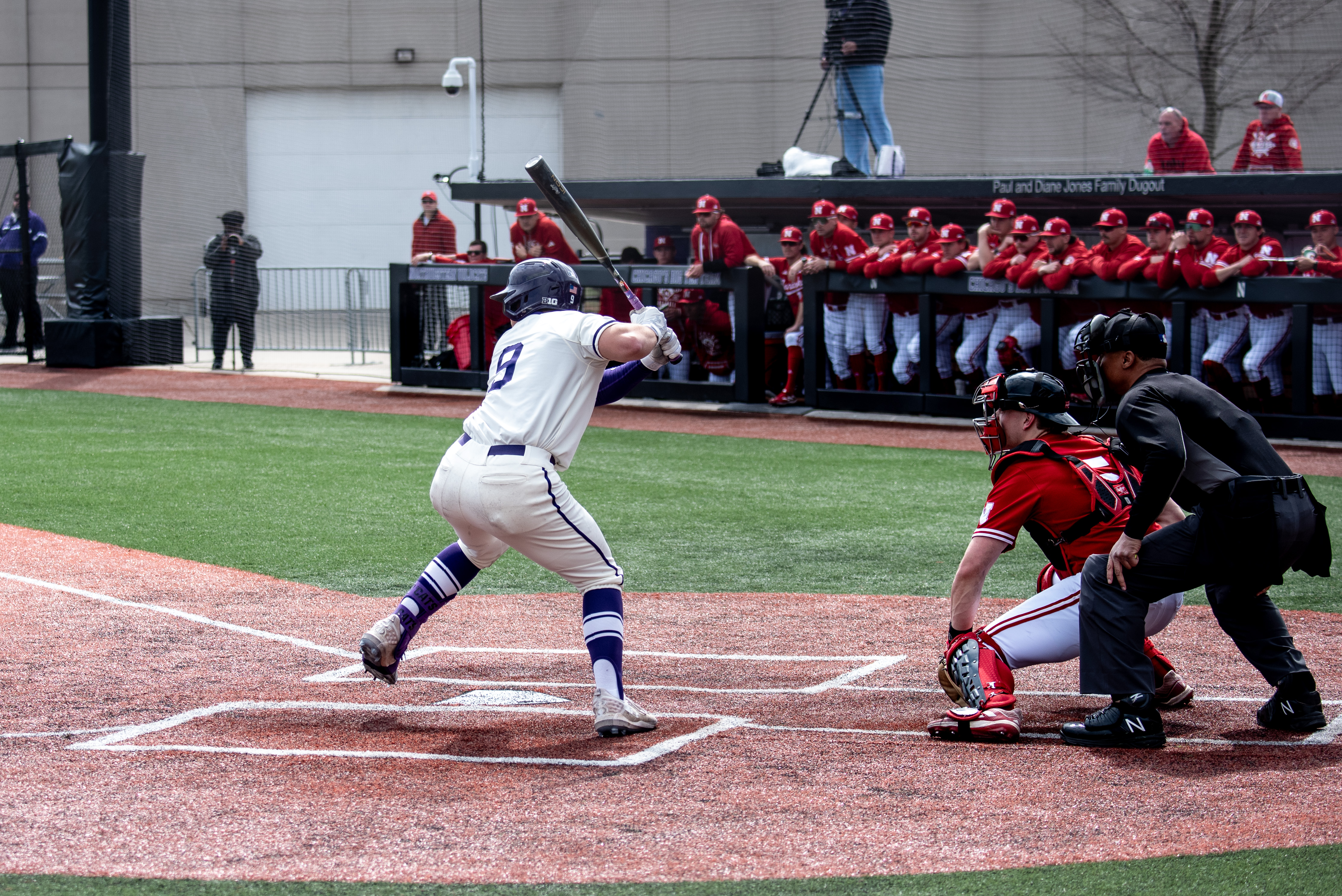 An athelete in white jersey holds a baseball bat with the gloves.